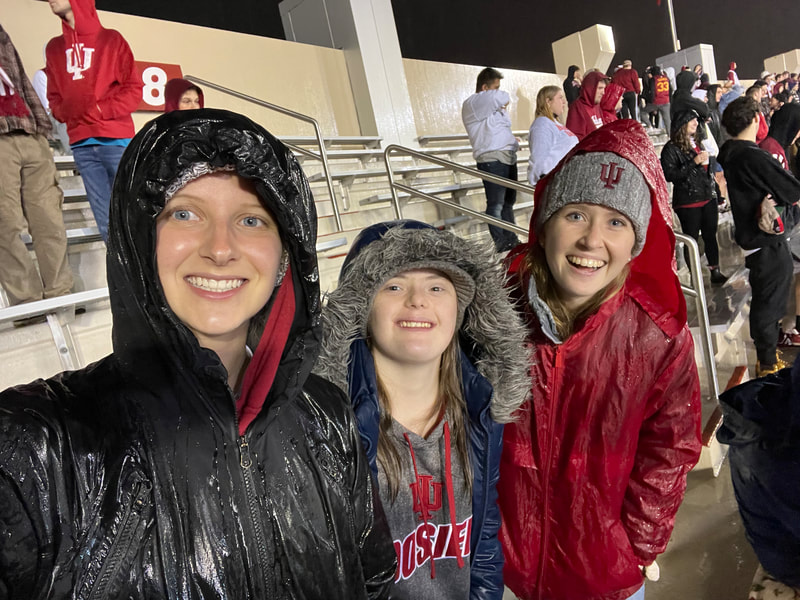 Madison standing on the football stadium bleachers with Mackenzie and Grace. They are smiling at the camera and soaked from the rain.